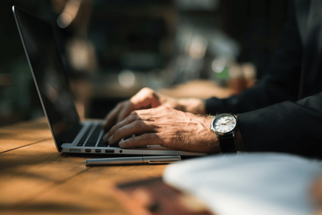 Professional working on a MacBook at a sunlit wooden desk with an elegant watch.
