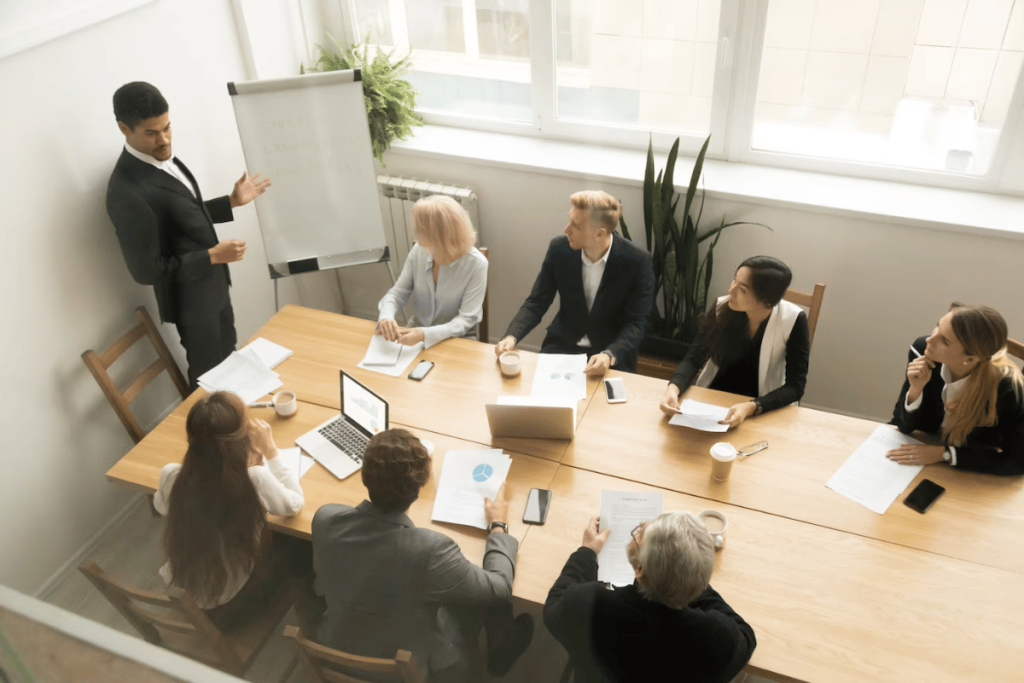 A group of people sitting around a table with a person giving a presentation.