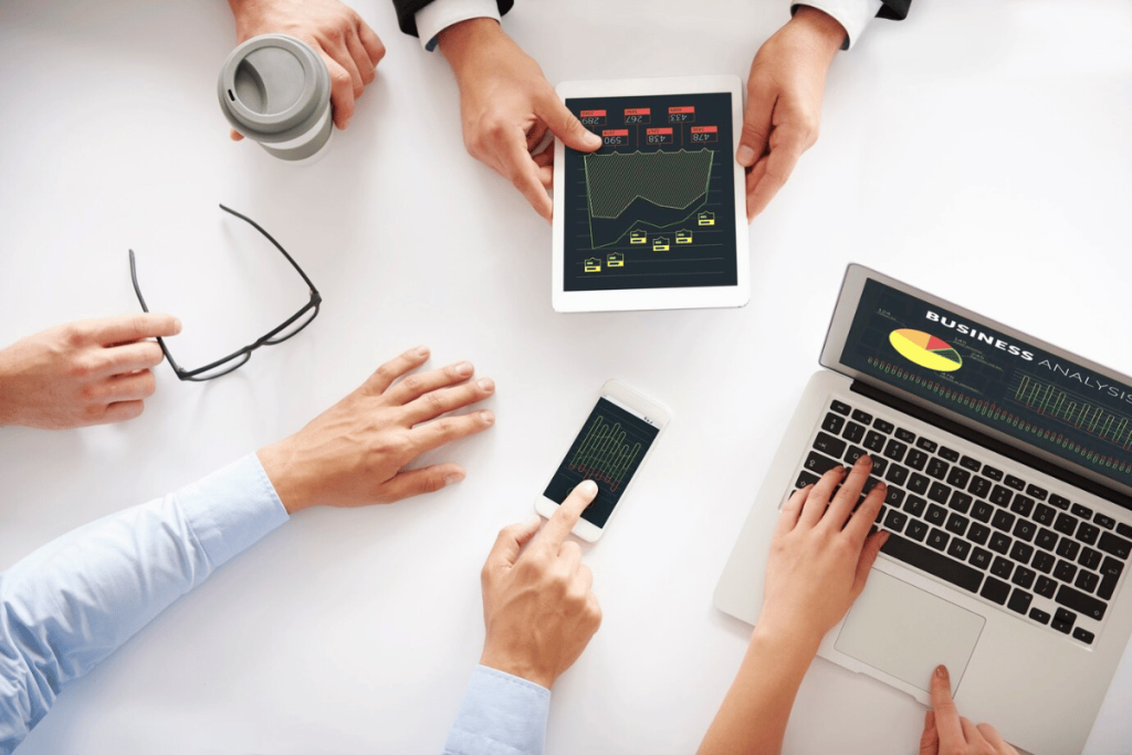 A group of people sitting around a table with laptops and tablets.