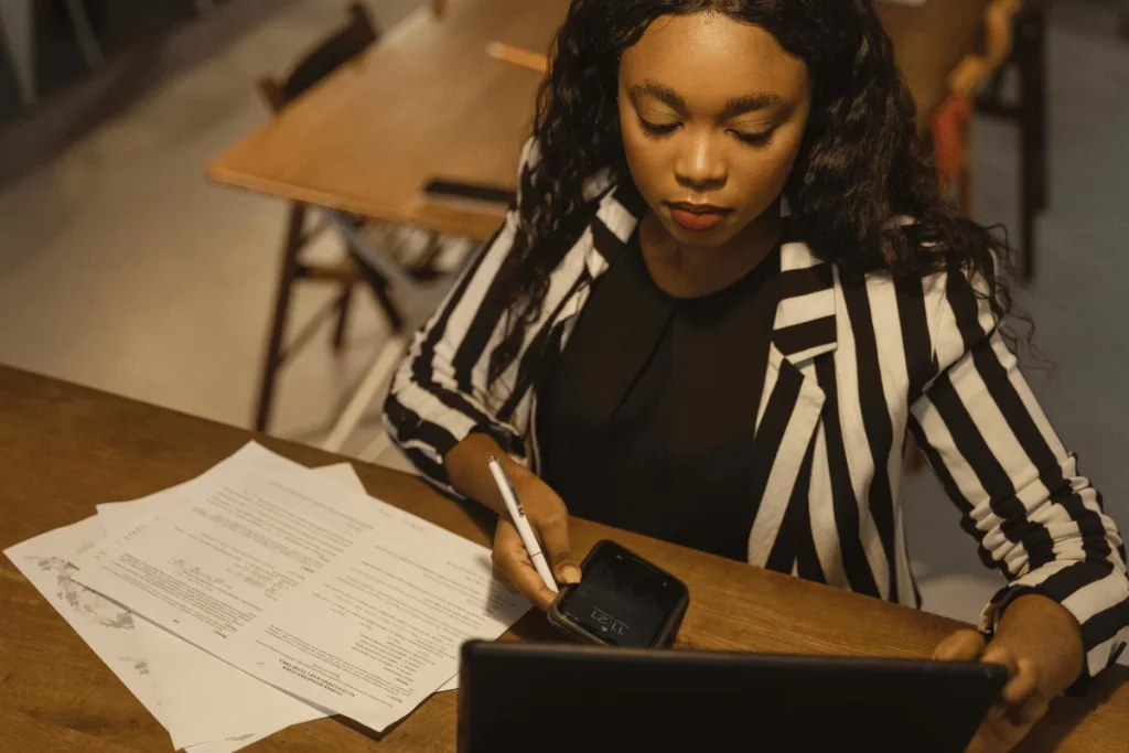 Dedicated female entrepreneur working on financial documents with mobile technology.