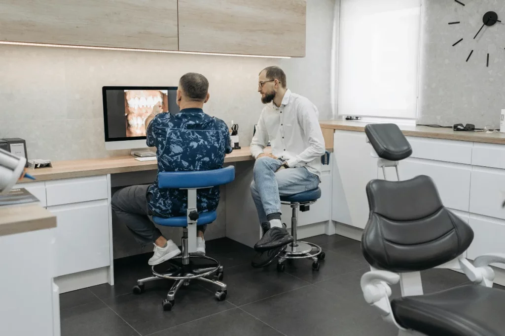 Two professionals in a dental office looking at dental X-rays on a computer screen.
