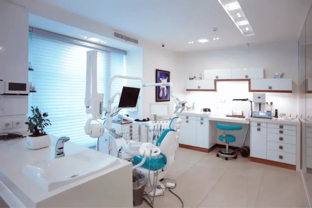 Modern dental office with white cabinetry, turquoise chairs, and dental equipment neatly arranged.