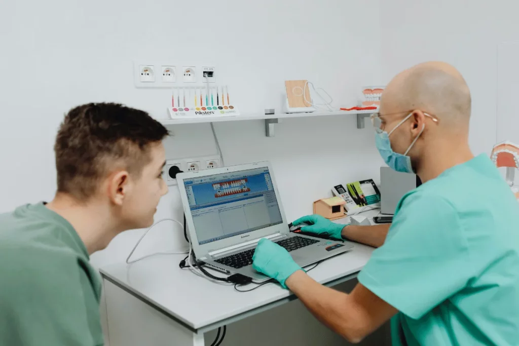 A dentist and a patient reviewing dental imaging on a laptop screen in a modern dental office.