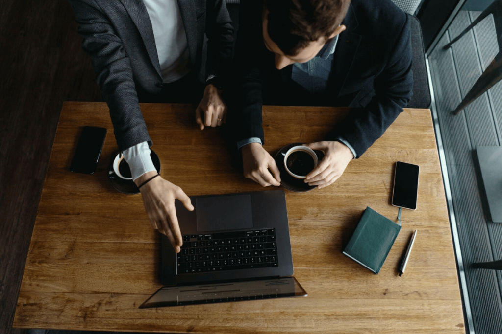 Two business people sitting at a table with a laptop and coffee.