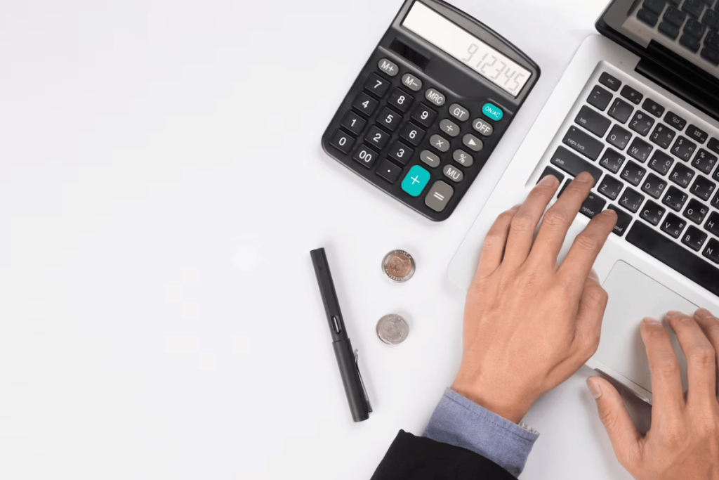 A person typing on a laptop with a calculator next to it.
