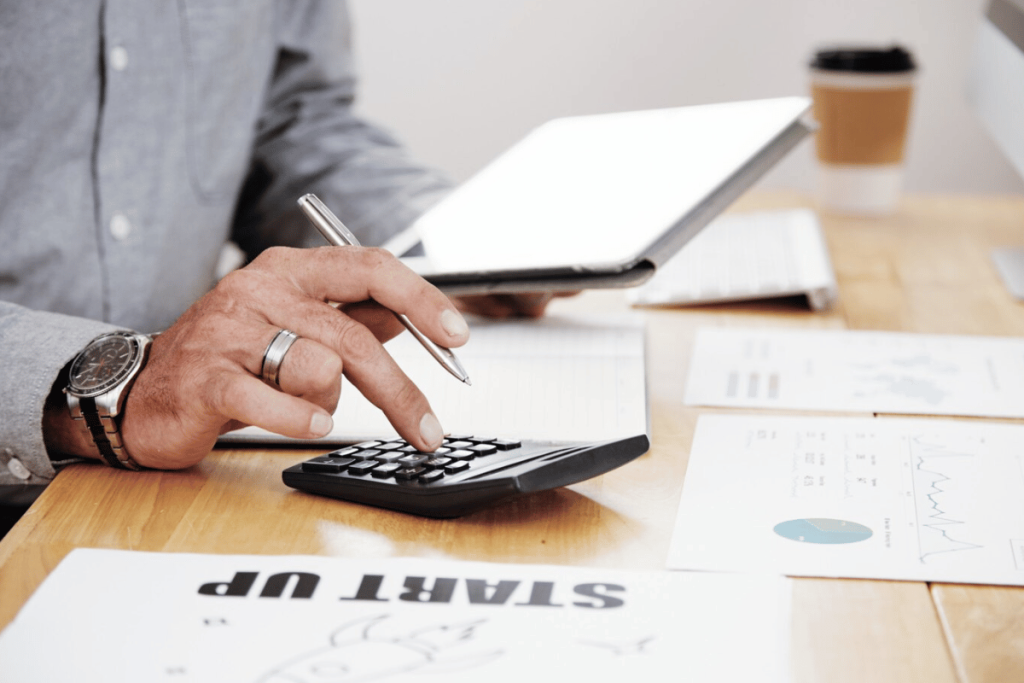 A person using a calculator to calculate the amount of money they need to invest in their business.