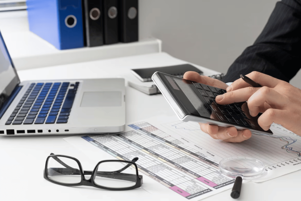 A person in a suit is using a calculator on their desk.