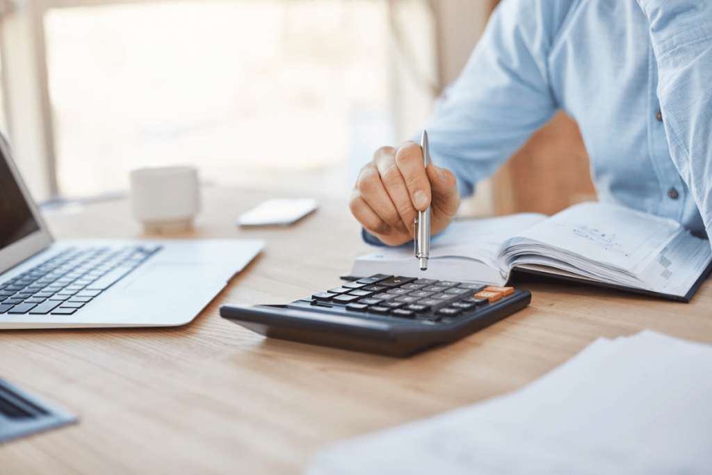 Businessman using calculator at desk with laptop and papers.