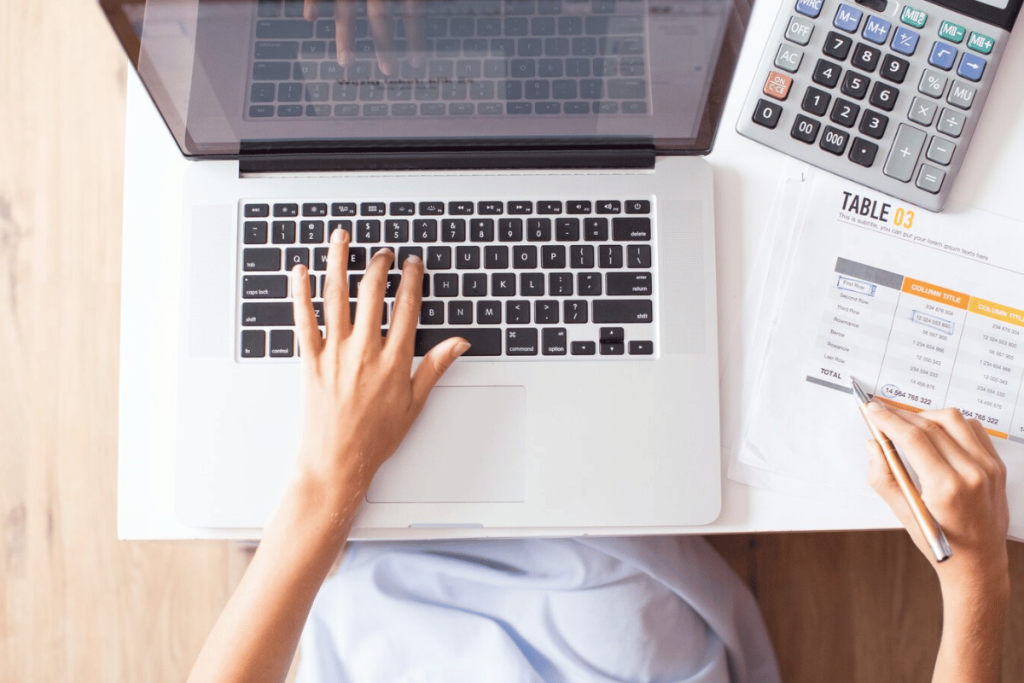 Top view of hands working on laptop with calculator and papers.