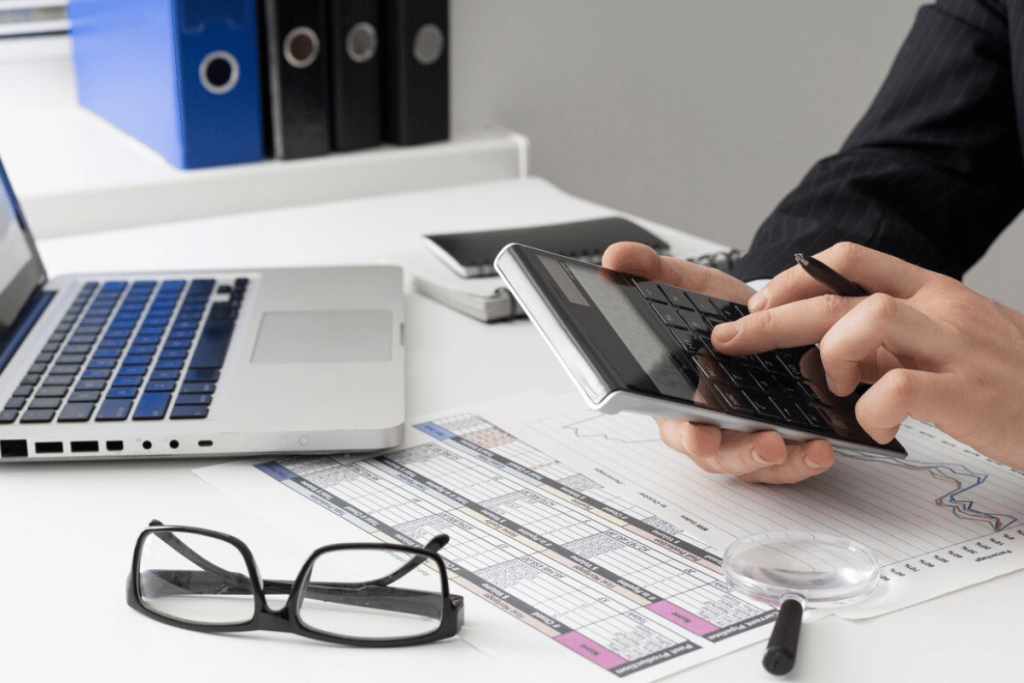A person in a suit is using a calculator on their desk.