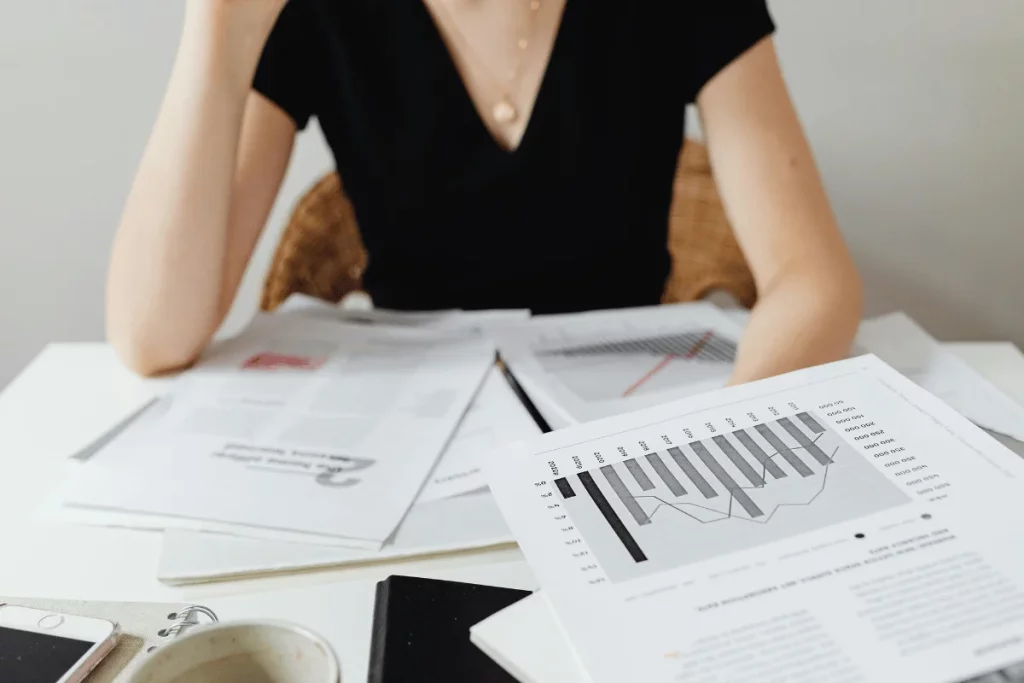 Person in a black shirt reviewing financial charts and reports spread out on a desk.