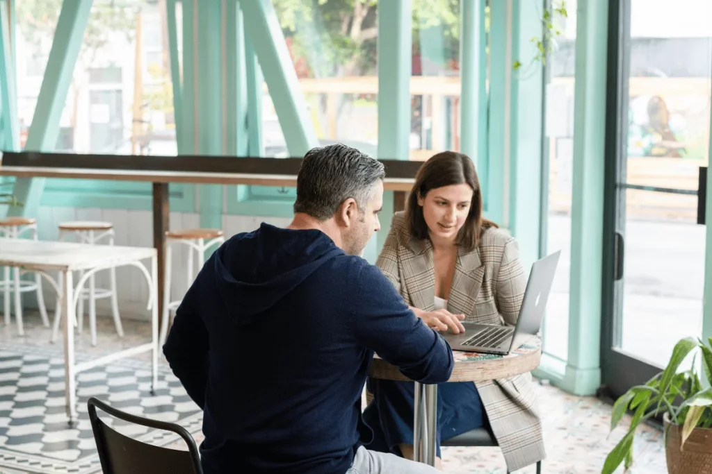 Business meeting between a man and a woman in a cafe, focused on a laptop screen.