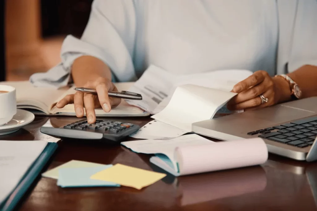 Person engaged in budget planning with a calculator on a wooden office desk.
