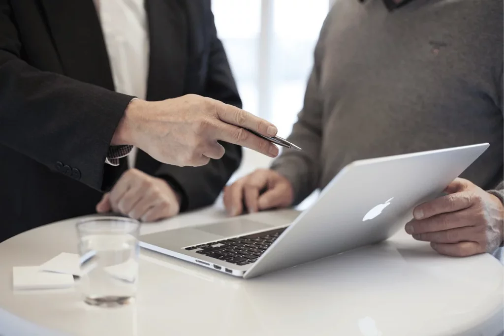 Professional discussion over an open MacBook, hands gesturing towards the screen.