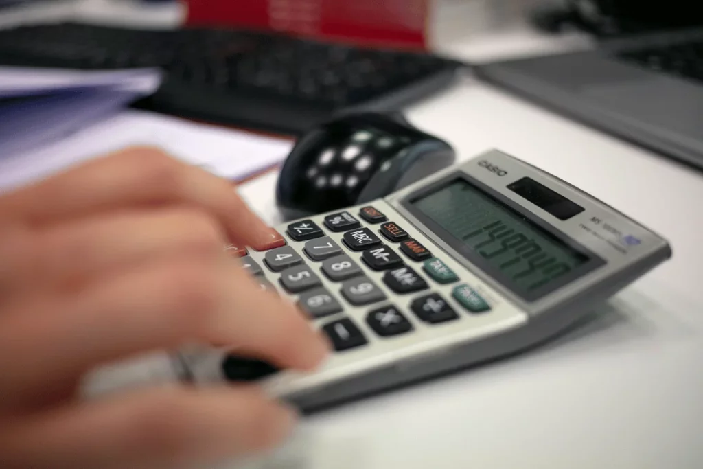 Person using a calculator with a mouse and computer nearby on the desk.
