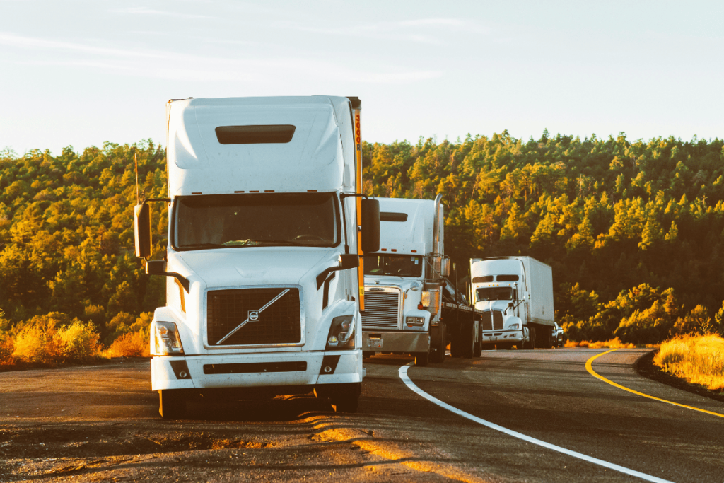 Semi-trucks driving along a scenic forest route during sunset.