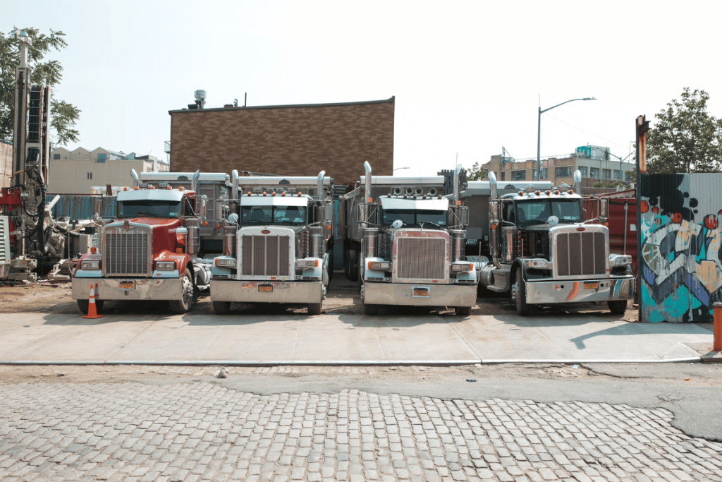 Semi-trucks parked in urban lot with construction equipment in background.