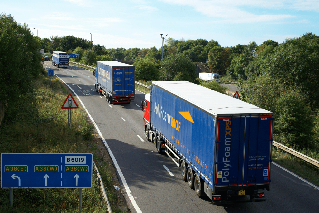 Fleet of lorries transporting goods on a sunny highway with clear directional signage.