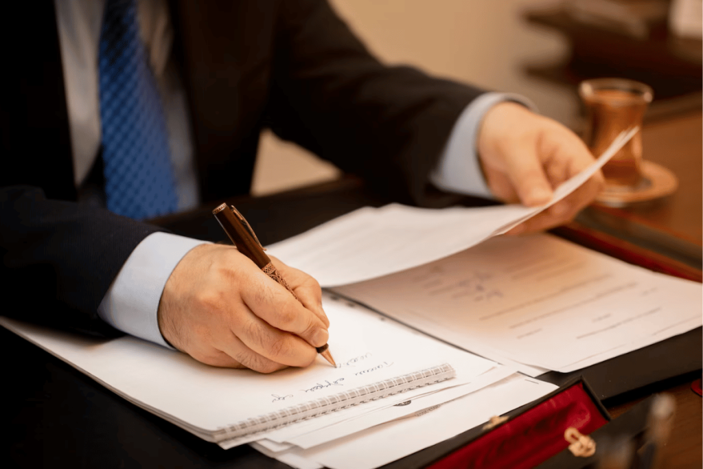 A person in a suit and tie sitting at a desk with papers and a pen.