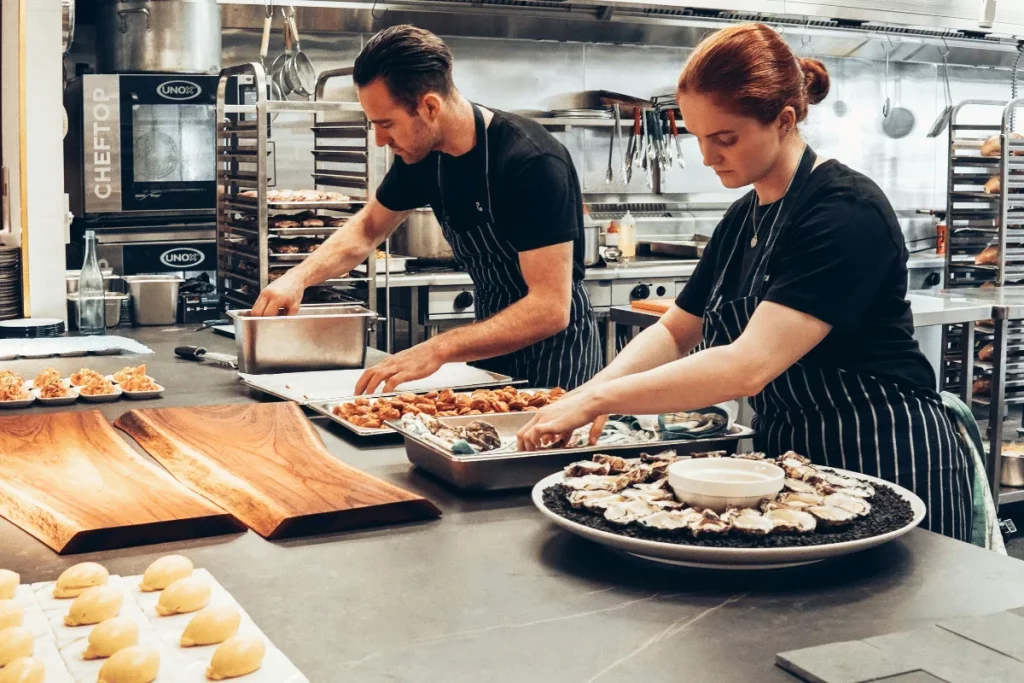 Two chefs in striped aprons preparing dishes in a commercial kitchen.