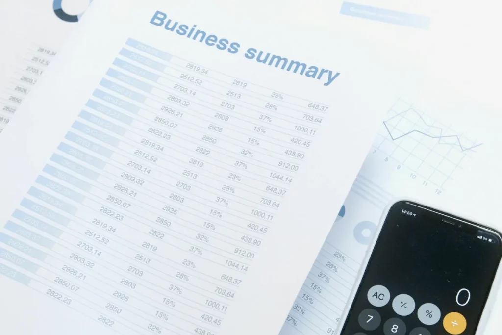 A business summary document with financial data and a smartphone calculator displaying '0' on a desk.