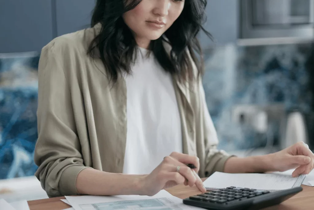 Woman using a calculator while reviewing financial documents at a desk in a modern office setting.