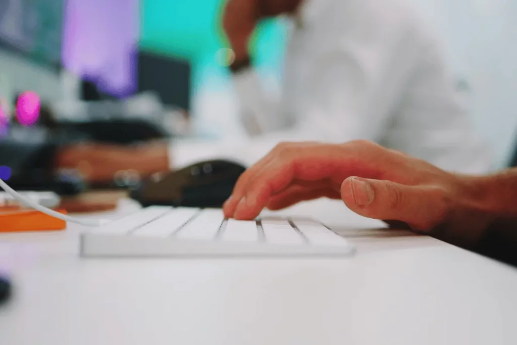 Detailed shot of hands working on a white keyboard, with a vibrant workplace backdrop.