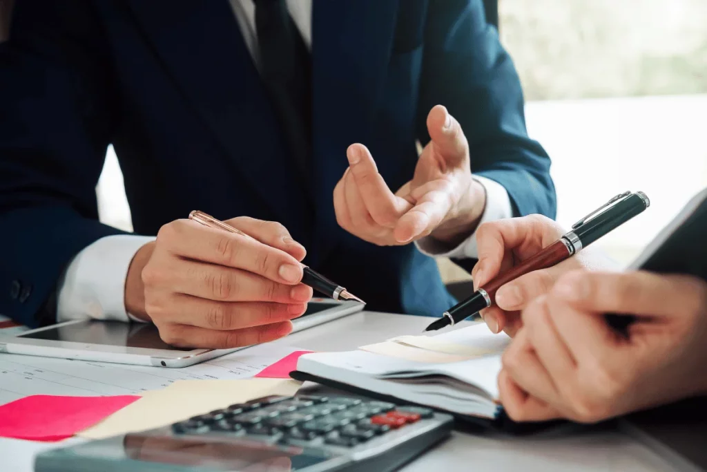 Close-up of business professionals discussing documents with pens and a calculator on the table.