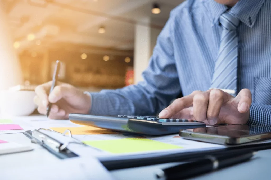 Close-up of businessman's hands using calculator on documents at a desk.