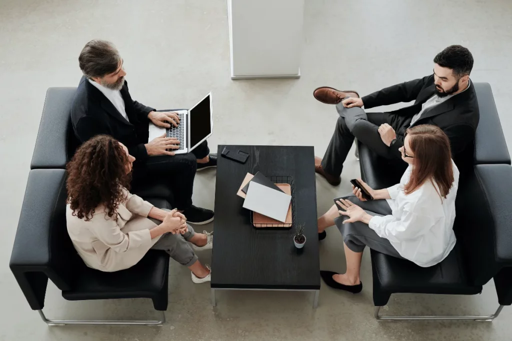 Colleagues in smart attire engaged in a discussion with laptops in a bright office.