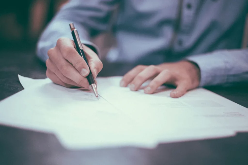 Person signing a document with a pen on a desk.