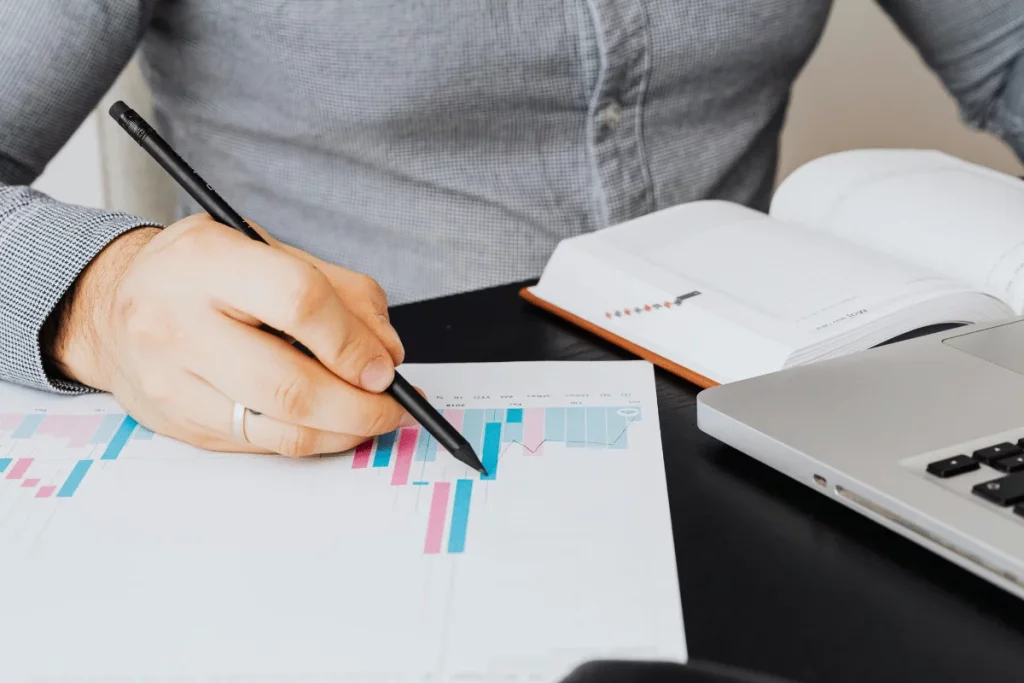 Person analyzing graphs with a pen, next to a laptop and notebook.