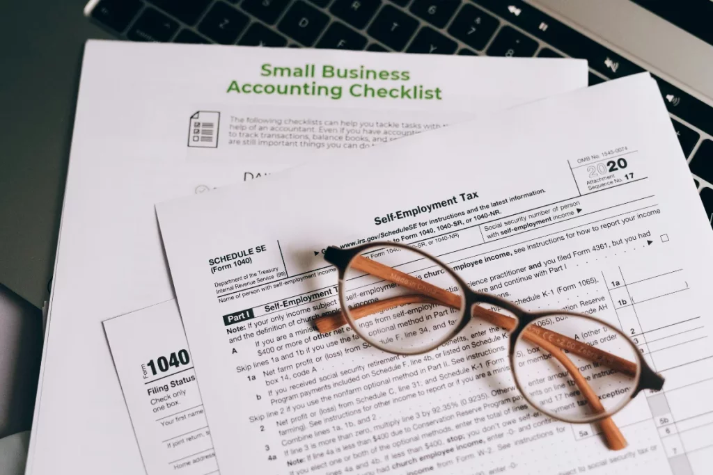 Self-employment tax forms and accounting checklist on a laptop keyboard.