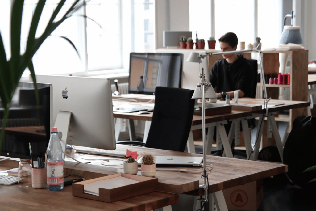 Open-plan office setting with iMacs, desk lamps, and potted plants.