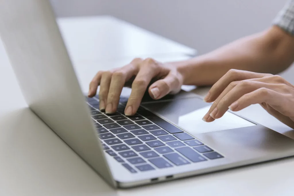 Close-up of hands typing on a laptop keyboard in an office.