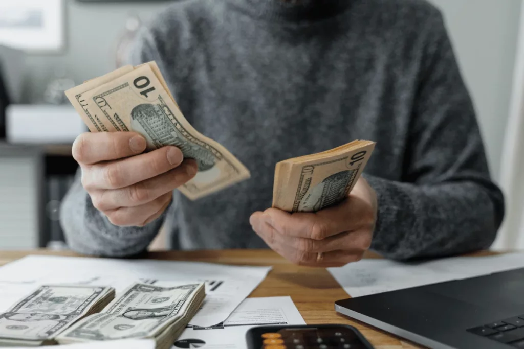 Hands holding and sorting through several twenty-dollar bills above a busy desk.