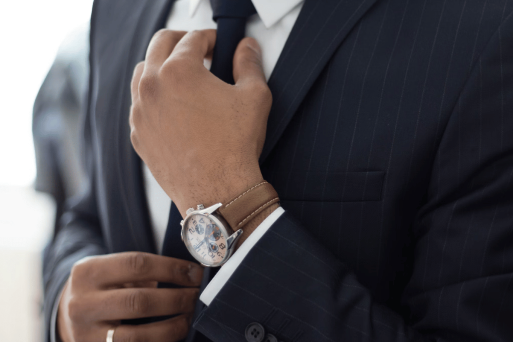 Elegant businessman fixing his tie, wearing a luxury watch on his wrist.