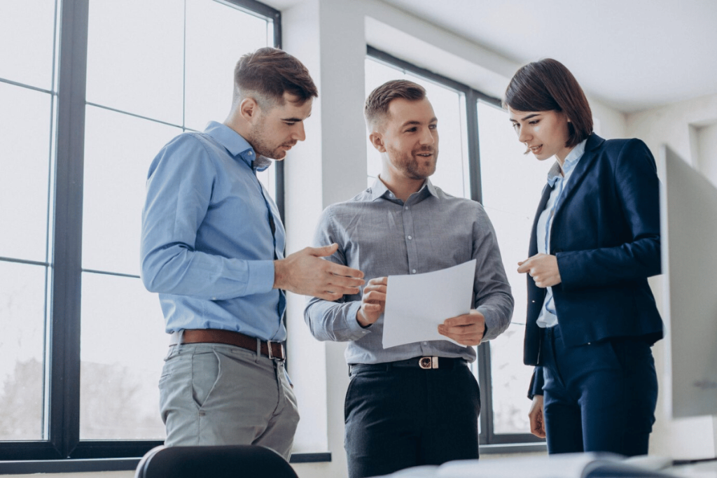 Three people standing in an office looking at a piece of paper.