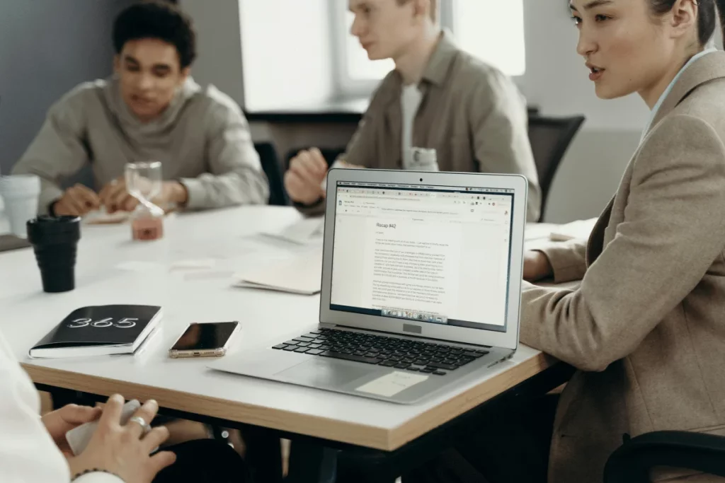 Business team in a meeting, with a laptop showing a document recap on a modern office desk.