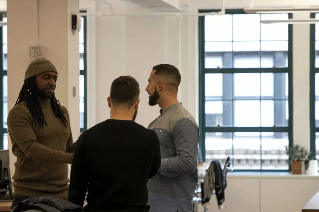 Three colleagues having a conversation in a modern office space with large windows.