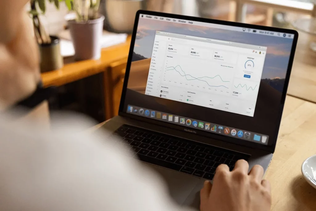 Over-the-shoulder view of a person analyzing financial data on a MacBook Pro.
