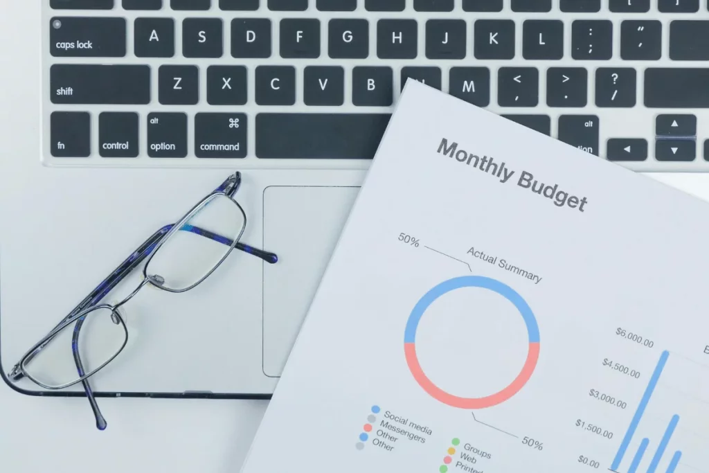 Monthly budget report with pie chart next to a laptop and glasses.