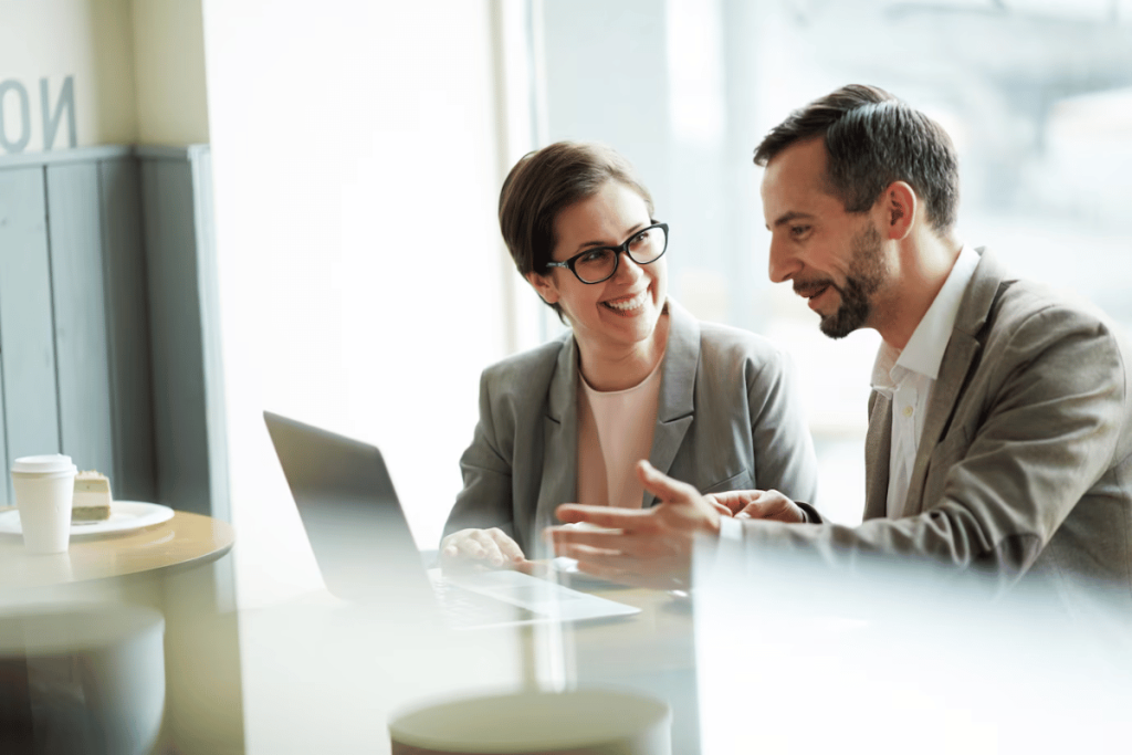 A person and another person sitting at a table with a laptop.