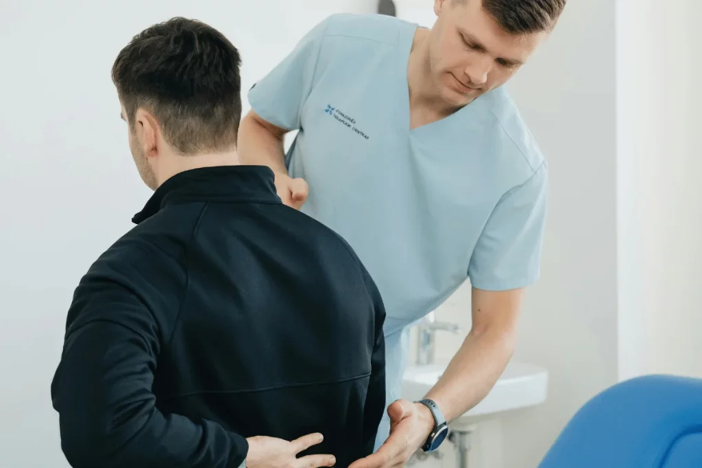 Physiotherapist evaluating male patient's lower back pain.