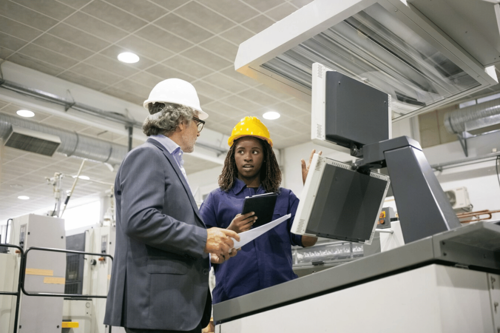 A person and another person in a factory looking at a computer.