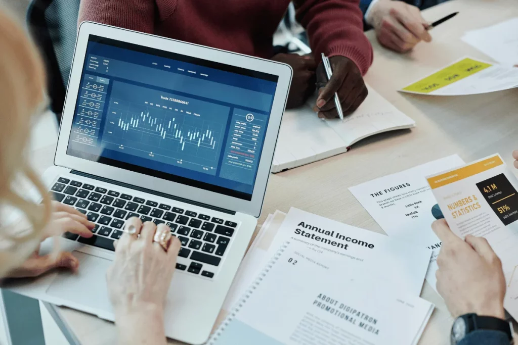 Group of people analyzing financial data on a laptop with reports and charts, including an annual income statement.