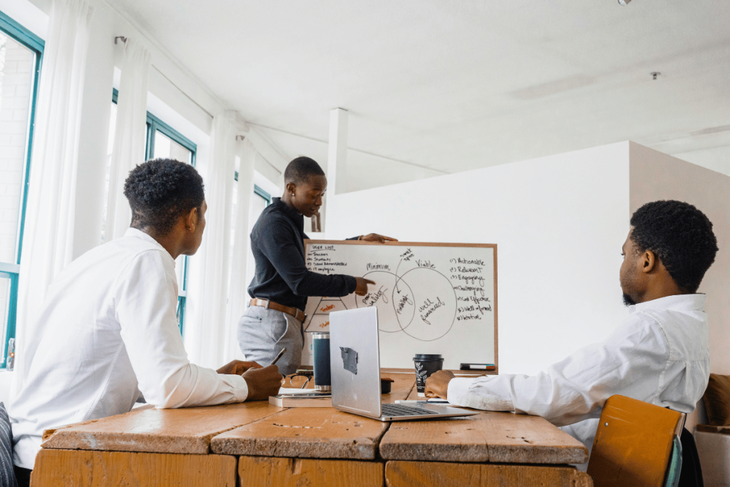 Three colleagues engaged in a brainstorming session with a whiteboard and laptops in a bright office.