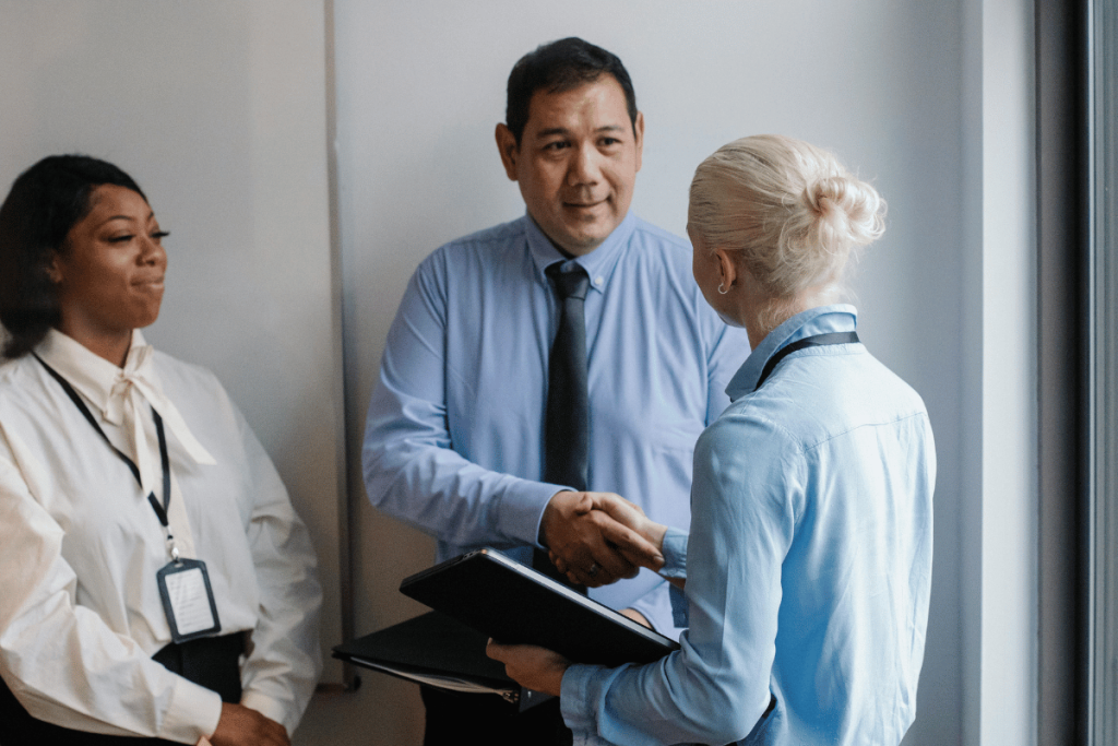 A man and woman in business attire shaking hands in an office hallway.