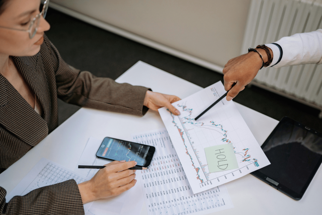 Two professionals examining financial charts and data on paper with smartphones.