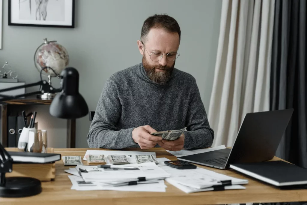 Man handling cash at a desk with financial documents and a laptop.